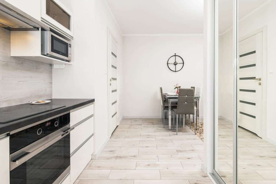 View of a small kitchen with a minimalist design. It features white cabinets, a black countertop, and a built-in stove and oven, focusing on practicality and space efficiency.