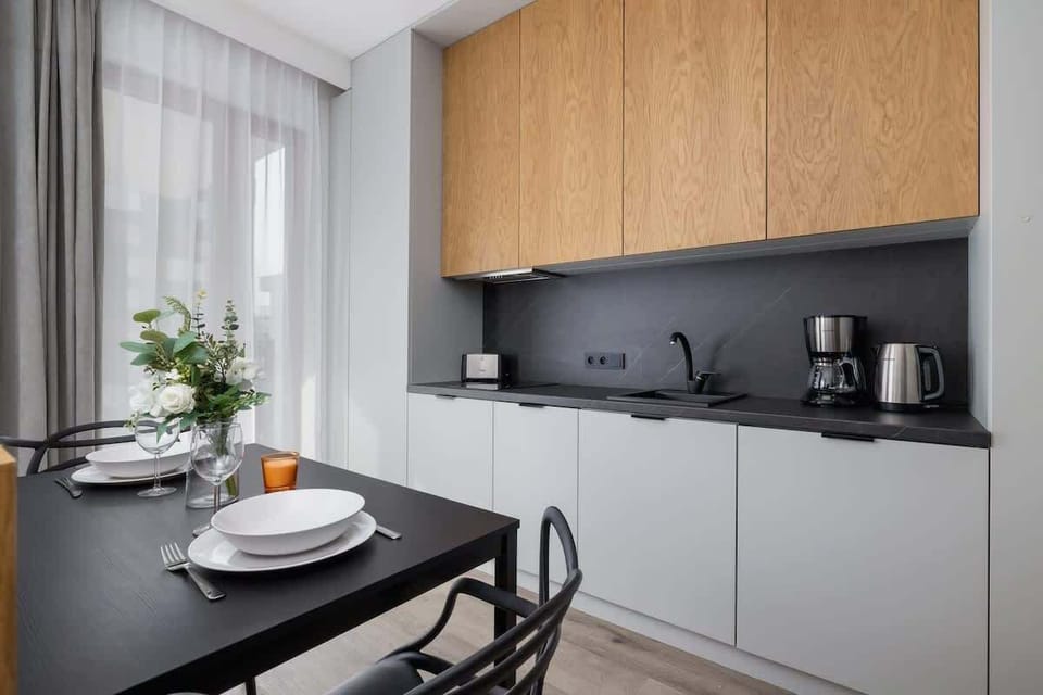 A sleek kitchen with black countertops, wooden cabinets, and a minimalist dining table setup.
