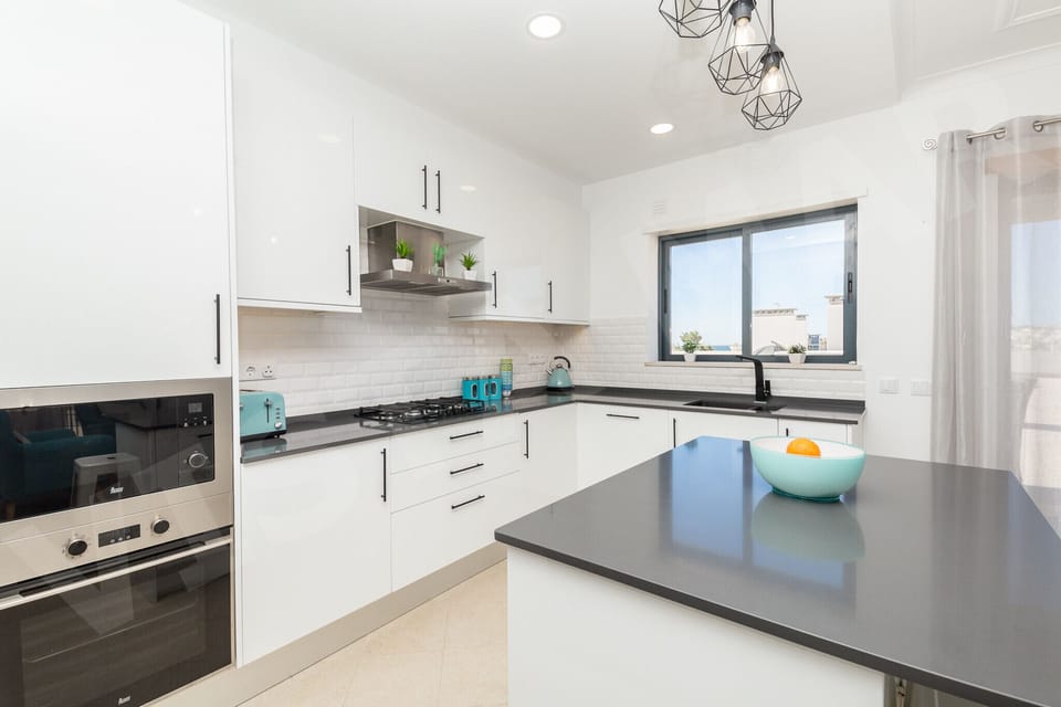 Bright and modern kitchen in Apartment Vista Mar, Lagos, with white cabinetry, subway tile backsplash, dark worktops, and natural light from the window, ideal for preparing meals during your Algarve holiday