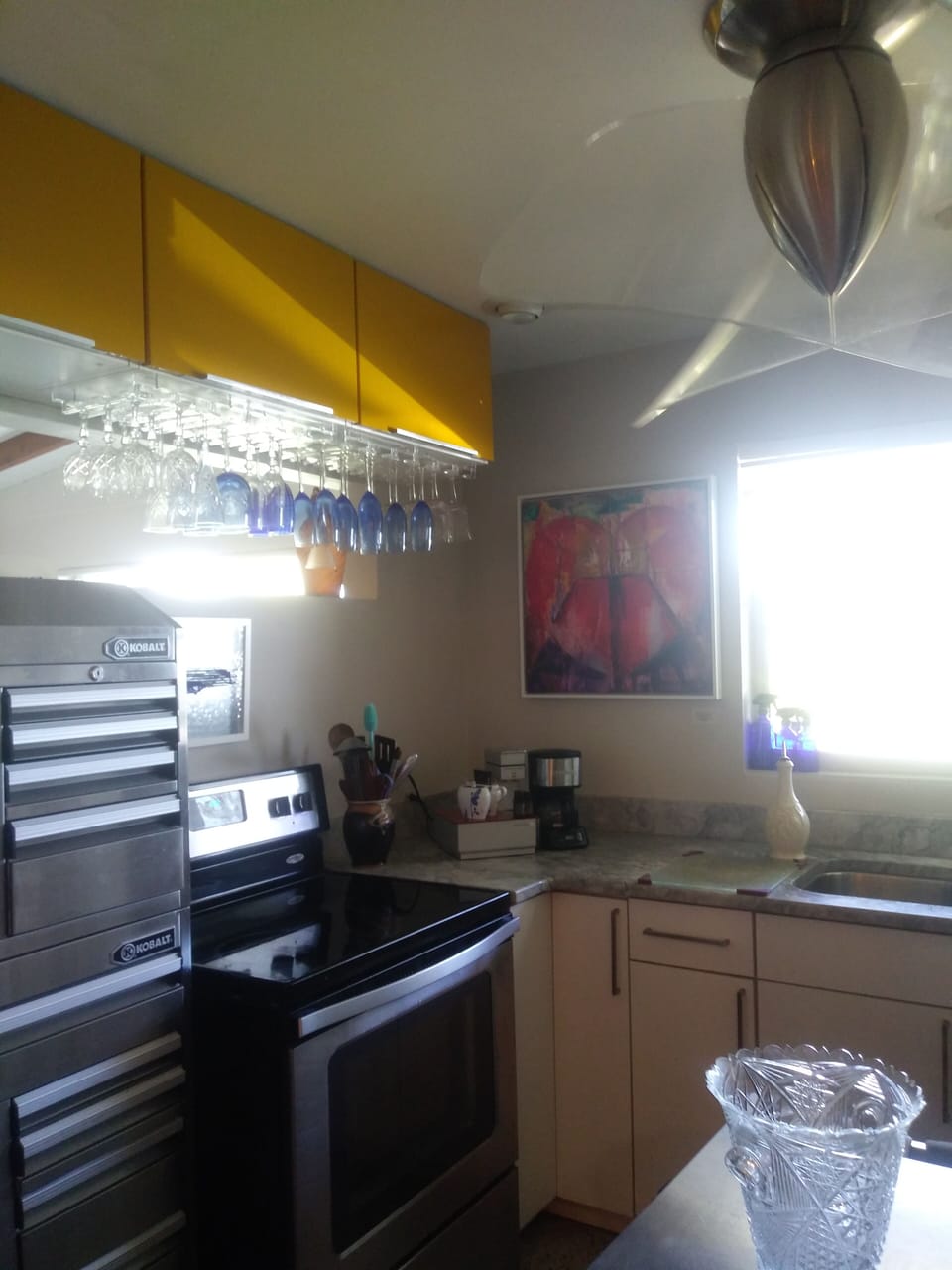 Left side of kitchen with upper cabinets, storage tool box, stove & double sink.