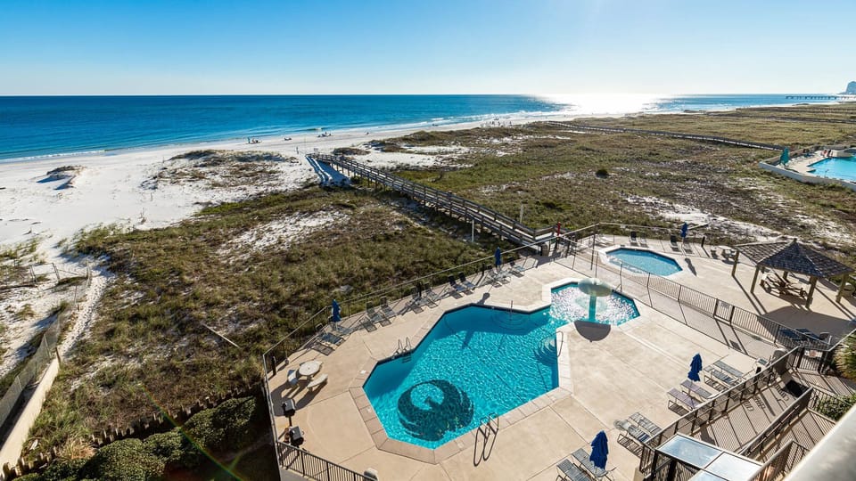 Expansive beach front view showcases a serene pool area with seating, leading to the inviting white sand beach
