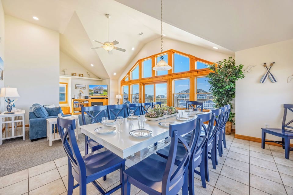 Gather at your spacious dining table beneath soaring vaulted ceilings, where sunlight pours through stunning arched windows framing peaceful waterfront views—perfect for memorable meals together.