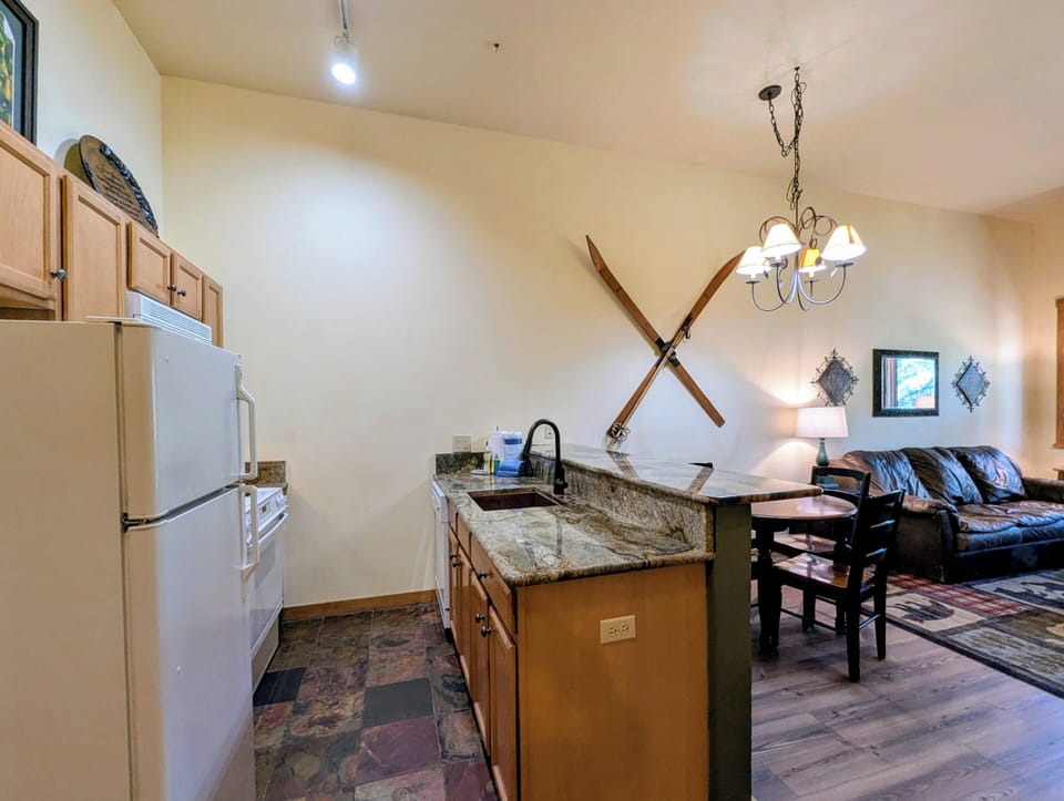 Your open-concept retreat blends mountain charm with modern comfort, featuring a fully-equipped kitchen, dining nook, and cozy living space beneath soaring vaulted ceilings.