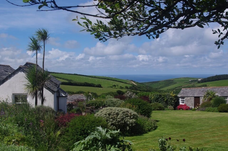 View of fields and sea, house on left and stone outbuildings below and on right.