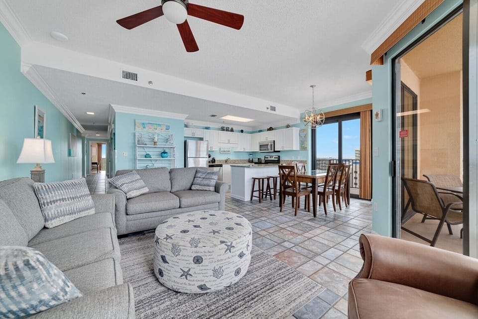 Luminous living area featuring a gray sofa with queen sleeper and a dining table with beach-inspired accents and views
