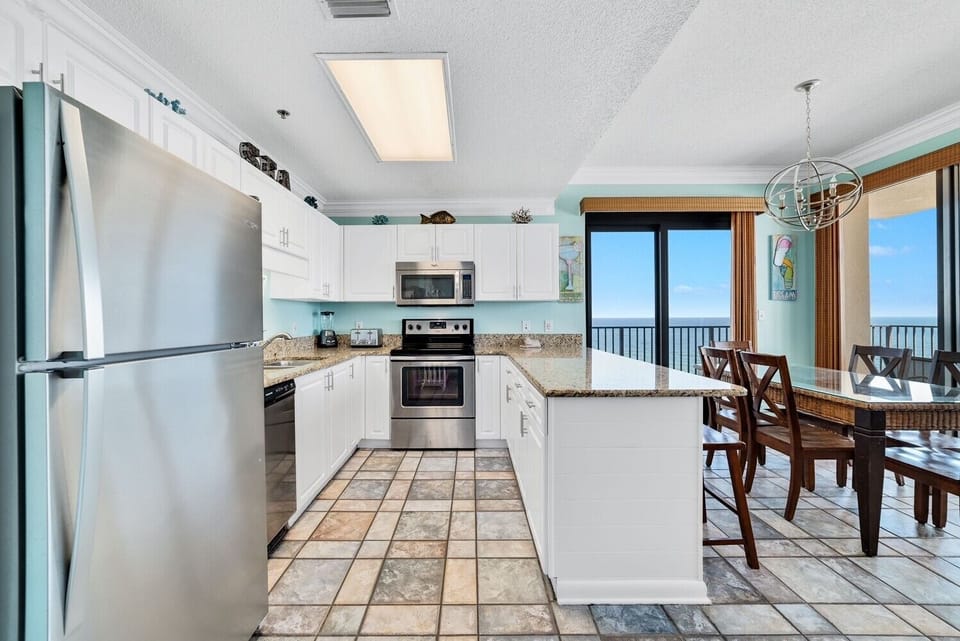 Bright and airy kitchen features white cabinetry, granite countertops, stainless appliances, and a view of the beach