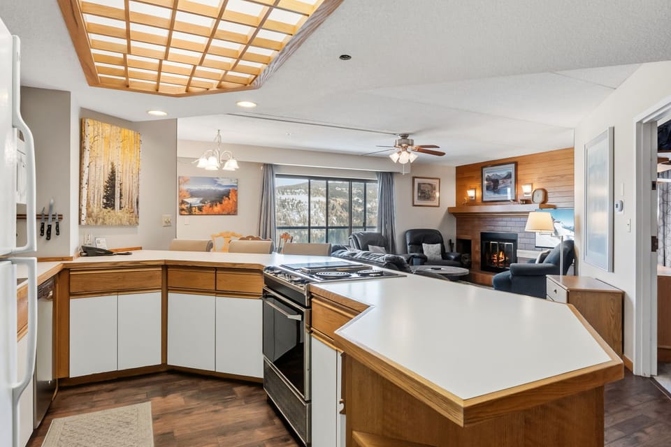 Your spacious open-concept retreat features a fully equipped kitchen flowing into a cozy living area with fireplace and mountain views.