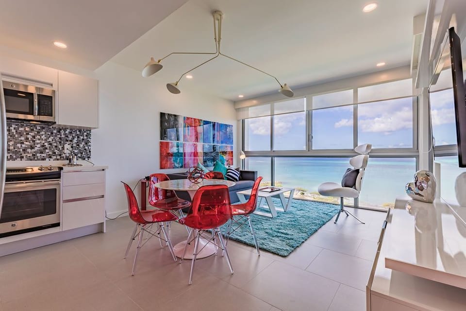 Bright open-plan living with vibrant artwork and stunning oceanfront views. The modern kitchen flows into a cozy seating area—perfect for your morning coffee ritual overlooking endless blue horizons.