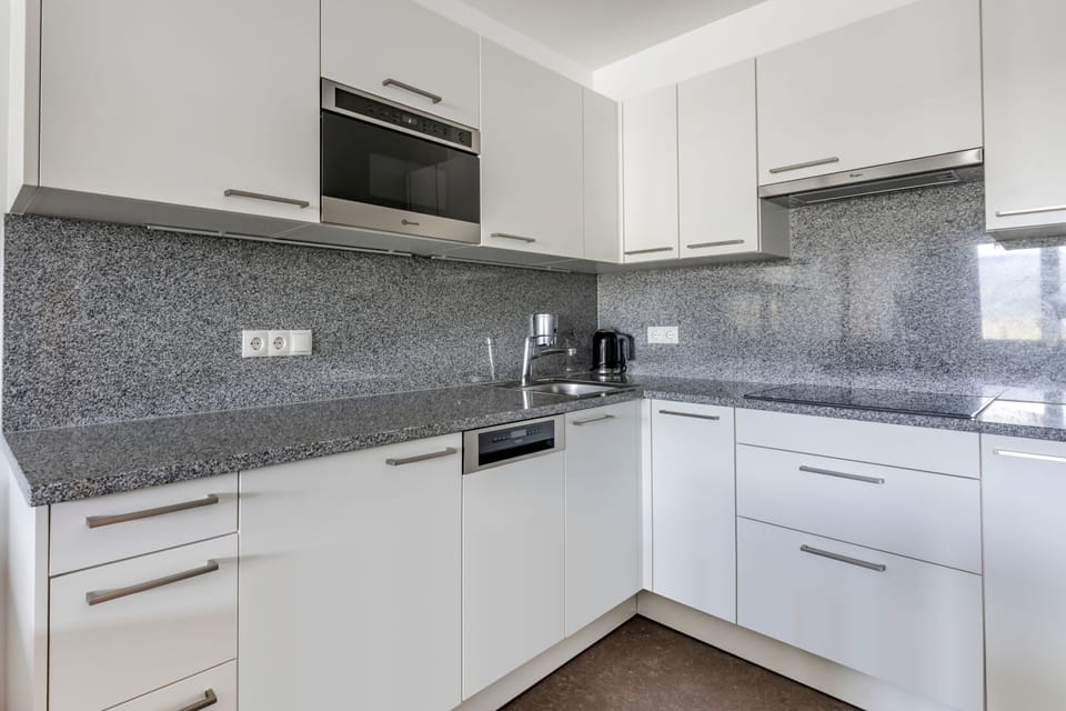The fully equipped kitchen boasts sleek white cabinetry, a granite countertop, a stove, and a coffee machine, creating a perfect space for cooking and entertaining.
