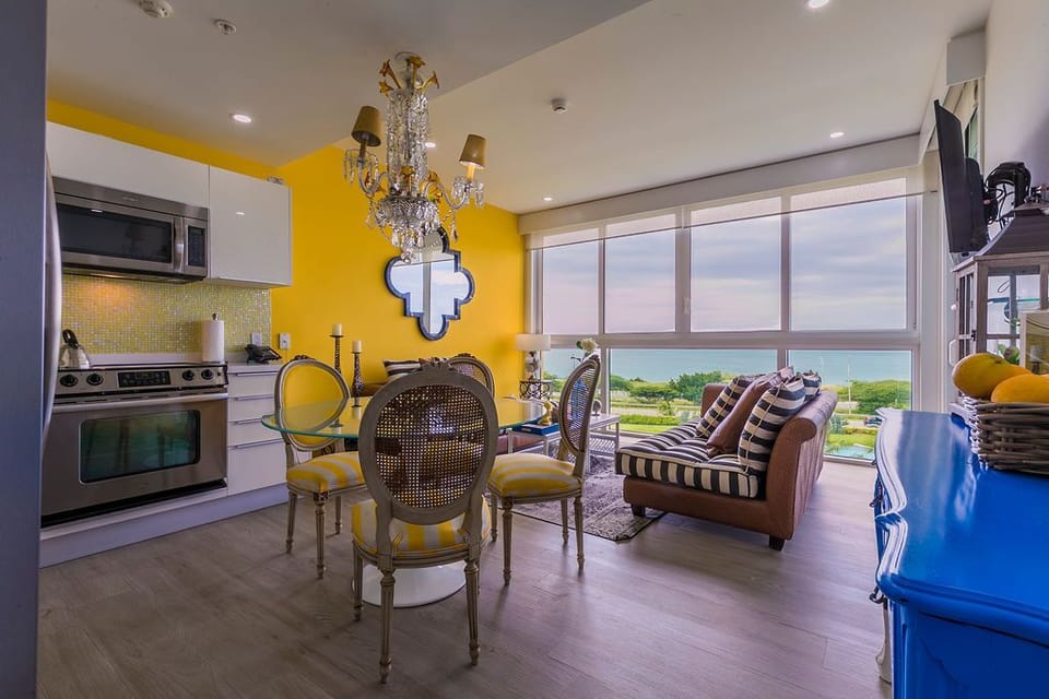 Picture yourself sipping morning coffee in this vibrant open-concept space, where cheerful yellow walls and elegant furnishings blend perfectly. Your gaze drifts through expansive windows to lush coastal scenery beyond.