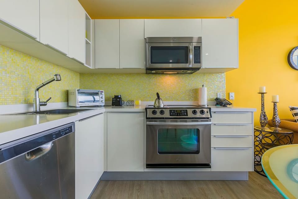 Step into your vibrant, fully-equipped kitchen featuring stainless steel appliances and a sunny yellow backsplash that brightens your culinary space every day.