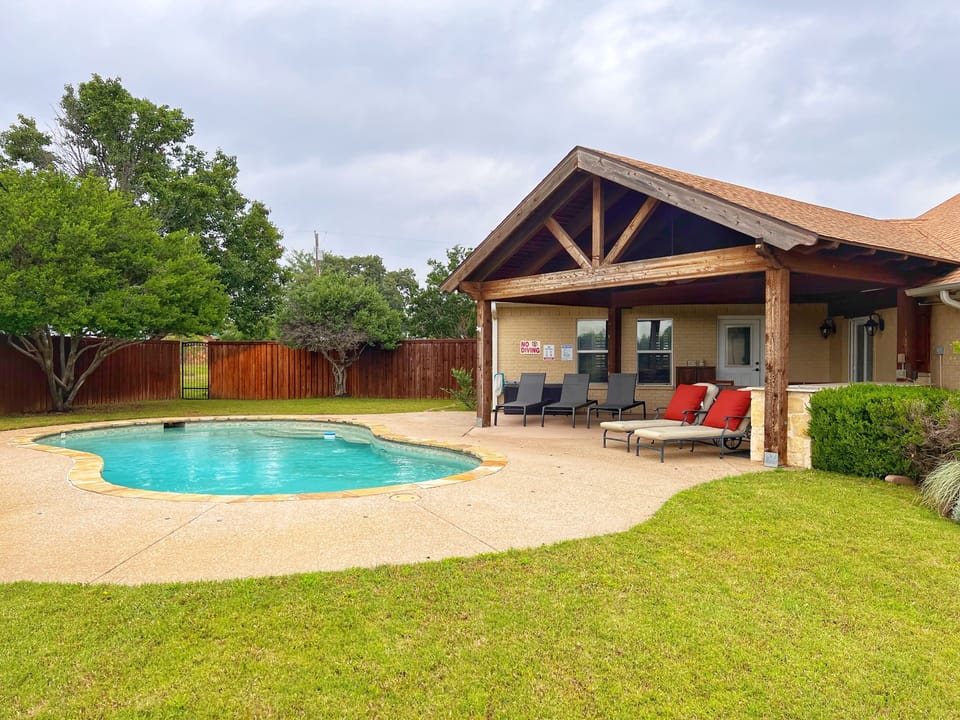 Fenced backyard with pool, covered patio, and sun loungers