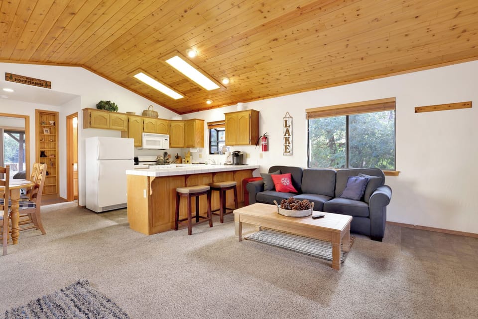 Cozy mountain living room with wood ceilings, stone fireplace, comfy seating, and smart TV—perfect for relaxing evenings, movie nights, and warm cabin vibes after outdoor adventures.
