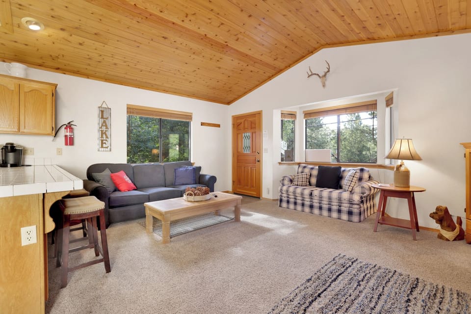 Cozy mountain living room with wood ceilings, stone fireplace, comfy seating, and smart TV—perfect for relaxing evenings, movie nights, and warm cabin vibes after outdoor adventures.