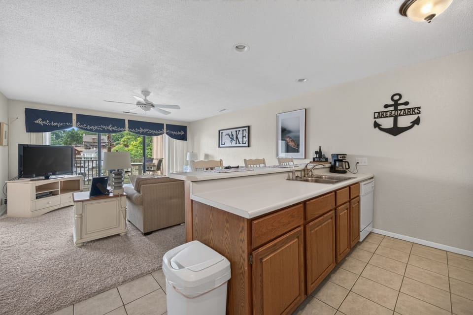 Relax in your open-concept living space where the kitchen flows seamlessly into the cozy living area, complete with lake-themed decor and a balcony overlooking the water.