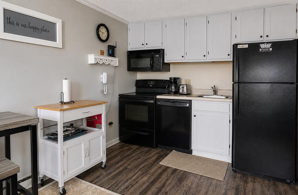 Kitchen with black appliances, white cabinets, wood-top rolling cart, and dark wood laminate flooring.