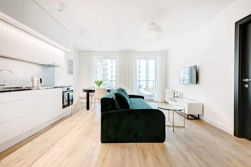 A similar view of the living room with the sofa, showing more of the open-plan layout. Behind the sofa is a kitchenette with white furniture. 