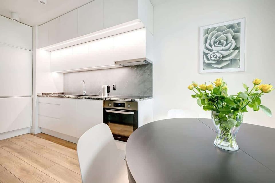 A dining area connected to the kitchen, with a round table, white chairs, and a vase with yellow flowers.