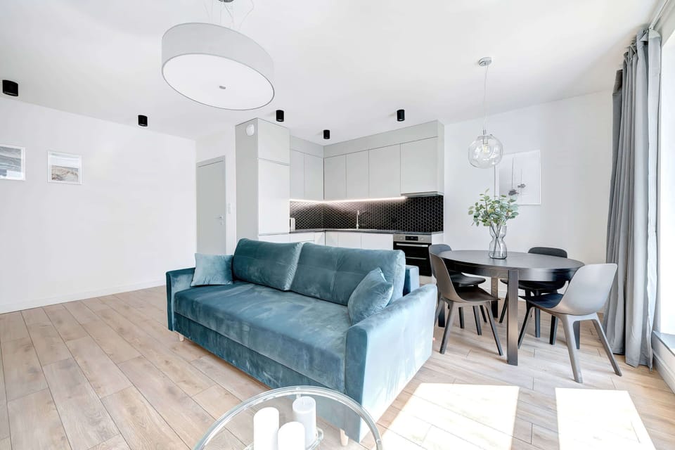 Another angle of the living room, showcasing the dining area, sleek kitchen cabinets, and a large TV on the wall.