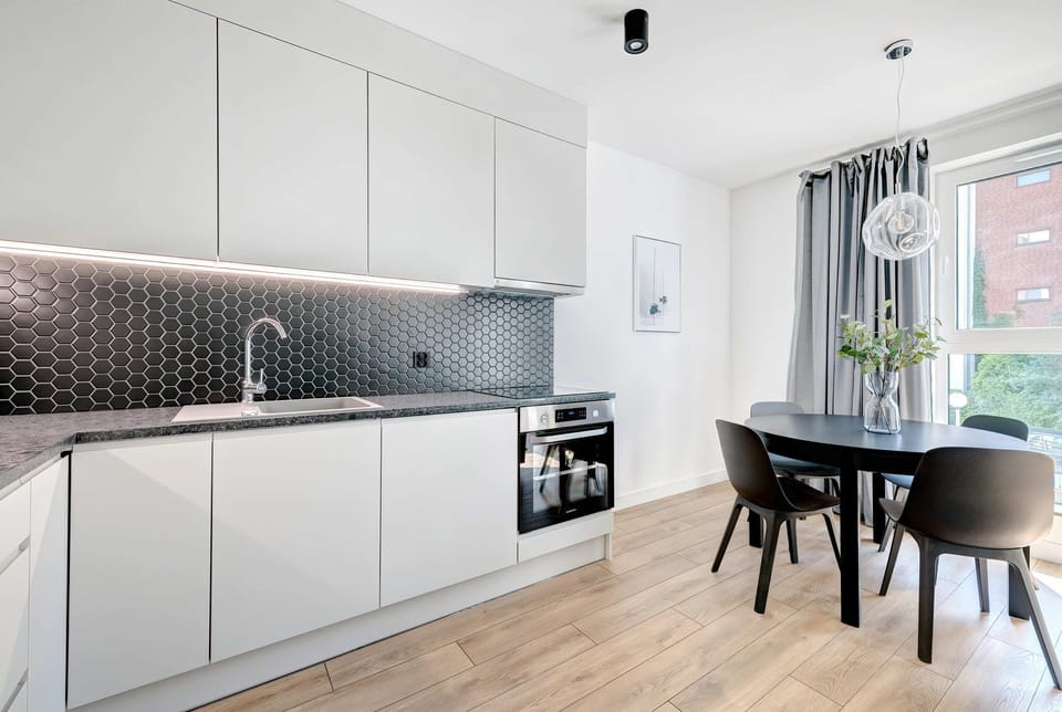 The stylish kitchenette, equipped with white cabinetry, black-tiled backsplash, and a dining table for two.