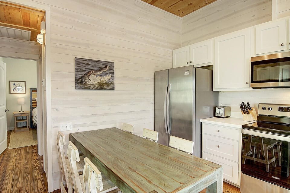 Your bright coastal kitchen features rustic wood paneling, modern appliances, and a weathered dining table perfect for morning coffee and meal prep.