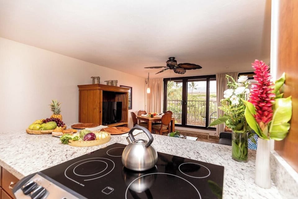 Functional kitchen featuring a sleek cooktop, granite counters, and a view into the bright living area with tropical décor