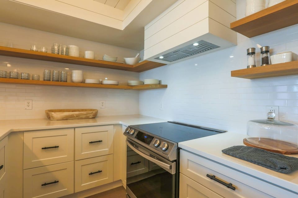 The spacious kitchen features a white tiled backsplash, floating shelves and white cabinets.