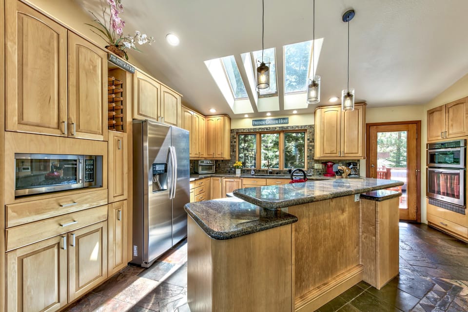 Granite-topped island sits beneath pendant lights and skylights in the kitchen with maple cabinetry and slate flooring.