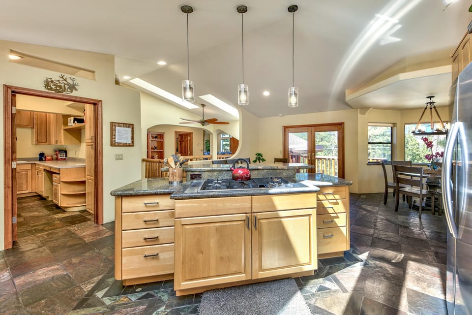 Kitchen island with granite countertop and gas cooktop, pendant lights above, and slate tile flooring throughout.