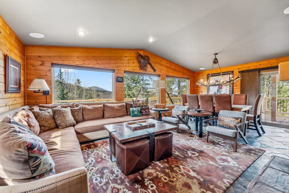 Living Room: L-shaped couch, 2 chairs, TV, decorative fireplace, large windows framing beautiful views, connected to dining room