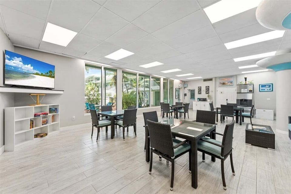 Clubhouse lounge with stylish seating, smart TV, and floor-to-ceiling windows overlooking the tropical courtyard — perfect for games, socializing, or relaxing.