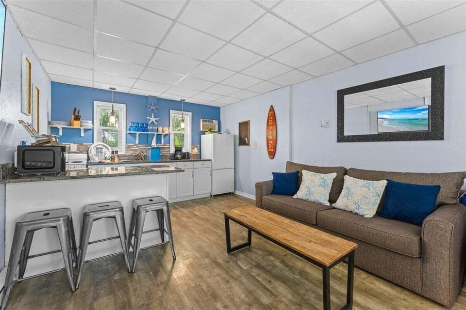 Bright living room with smart TV, ceiling fan, cozy sofa seating, and a pass-through bar to the kitchen — a relaxed coastal space to unwind after the beach.