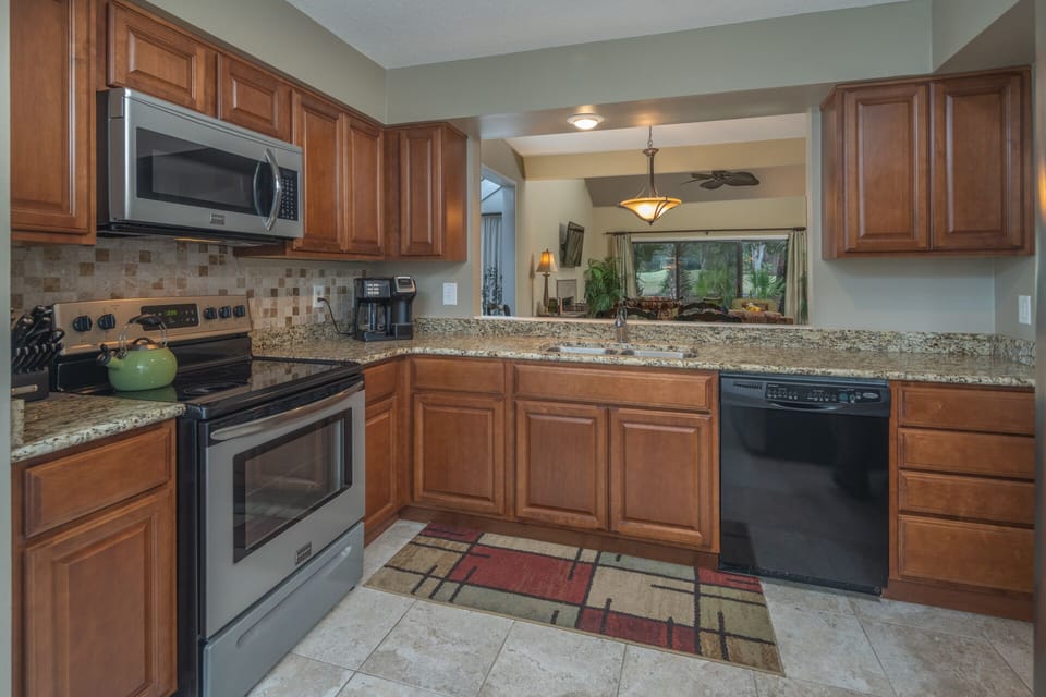 Warm wood cabinetry, granite countertops, and stainless steel appliances create a polished, well-appointed kitchen with generous prep space and a convenient pass-through to the living area.