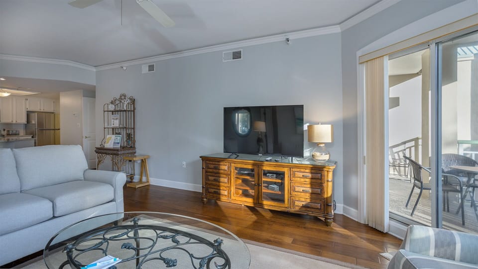 This bright living area offers a comfortable place to unwind, featuring hardwood floors, ample seating, and a large flat-screen TV with media console.