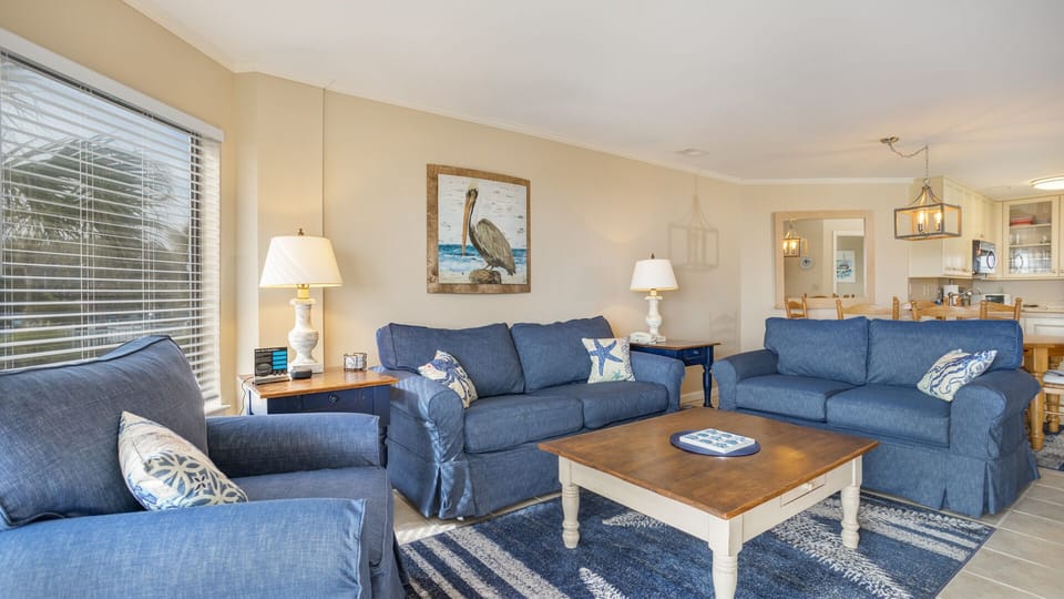 This bright and inviting living room offers a relaxing coastal feel with soft neutral furnishings, abundant natural light, and easy indoor–outdoor flow.