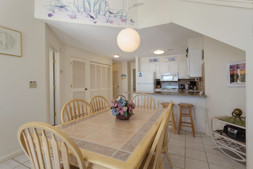 This light-filled dining area offers a comfortable gathering space with seating for six, set beneath a classic chandelier that adds a warm coastal touch.
