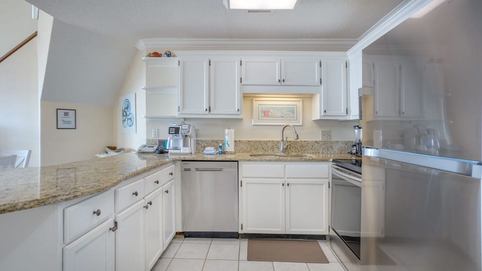 The kitchen features a spacious granite countertop, white cabinetry, and a full suite of appliances—providing plenty of room for meal prep and casual dining at the breakfast bar.