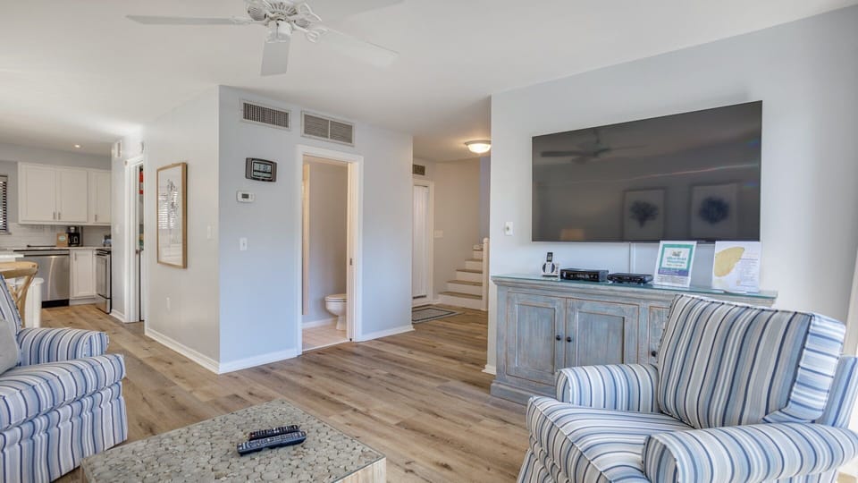 A wall-mounted TV anchors the room, while plush seating creates an inviting spot to unwind after a day at the beach or on the golf course.