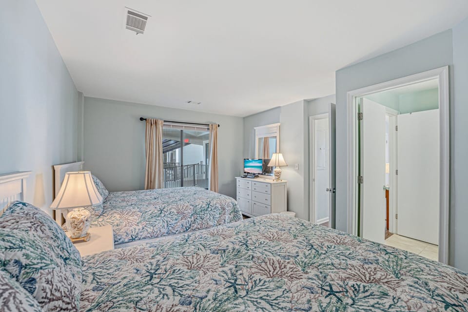 Spacious guest bedroom featuring two queen beds and direct access to the balcony.