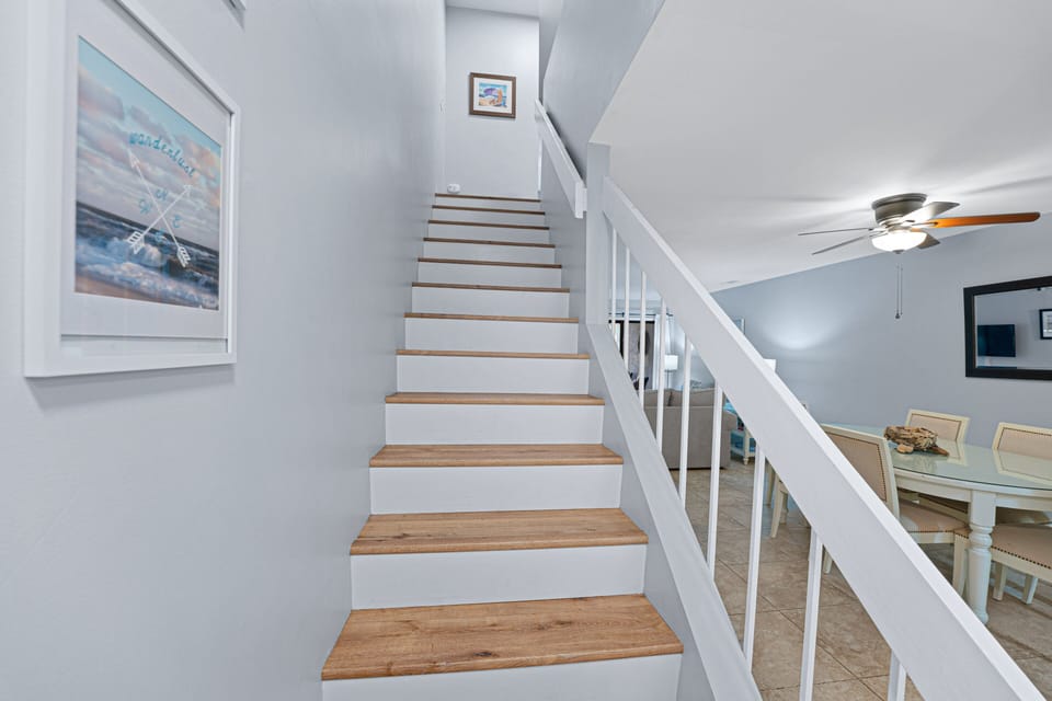 A bright staircase leads to the upper level, featuring fresh coastal tones and wood-look steps that add warmth to the space.