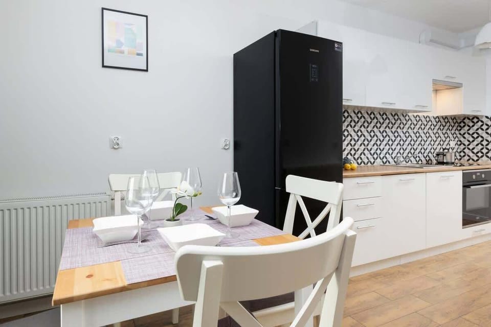 Simple dining space with white furniture and a black fridge in the background.