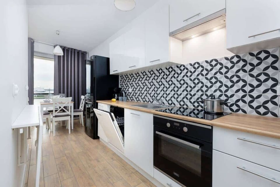 Modern kitchen with patterned backsplash, white cabinets, and wooden floor.