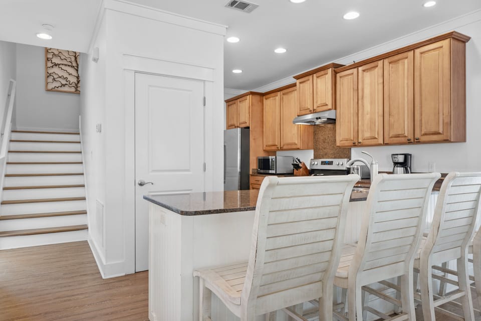 Inviting kitchen with bar seating, stainless appliances, and warm wood cabinetry—ideal for casual meals and morning coffee on your 30A vacation.