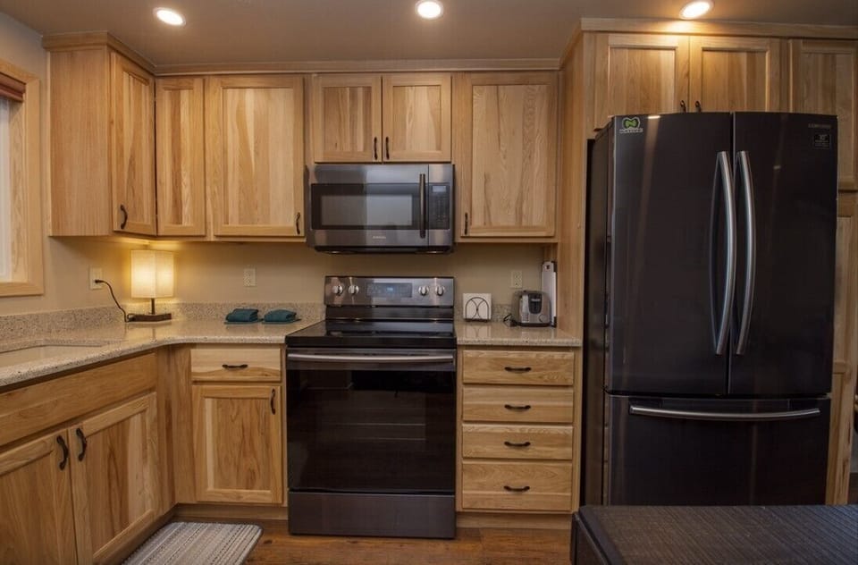 Your fully equipped kitchen invites culinary adventures with warm wood cabinets, granite counters, and modern black appliances ready for your cooking.