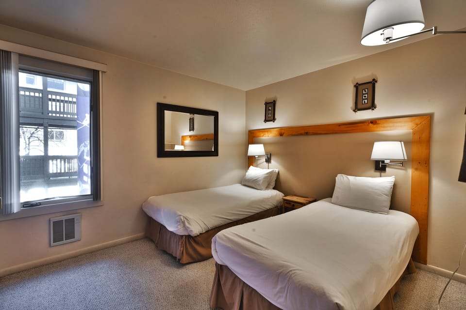 Guest bedroom includes two comfortable twin-sized beds, large mirror and wall mounted lamps above the beds