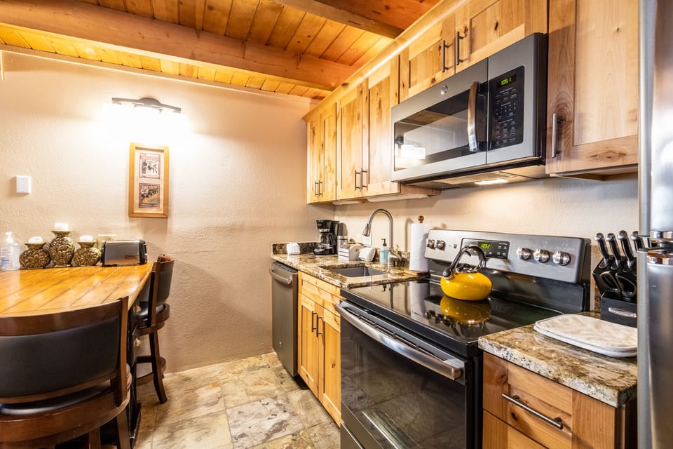 Your fully equipped kitchen invites home-cooked meals with granite counters, stainless appliances, and warm wood cabinetry under exposed beam ceilings.
