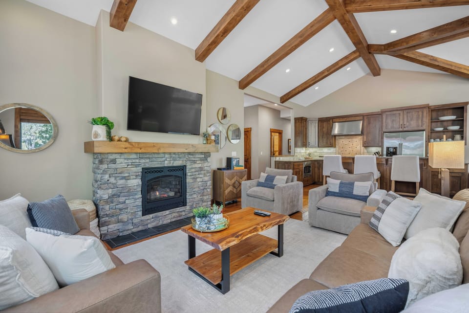 Curl up in this bright living room with soaring beamed ceilings, a cozy stone fireplace, and plush seating. The open layout connects you to the kitchen, perfect for unwinding after your adventures.