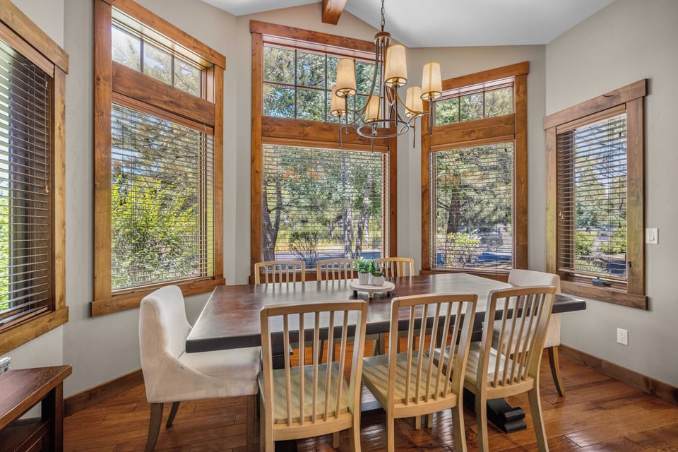 Gather around this warm dining table beneath soaring ceilings framed by rich wood beams. Sunlight pours through transom windows and custom woodwork, creating a welcoming space for your meals.