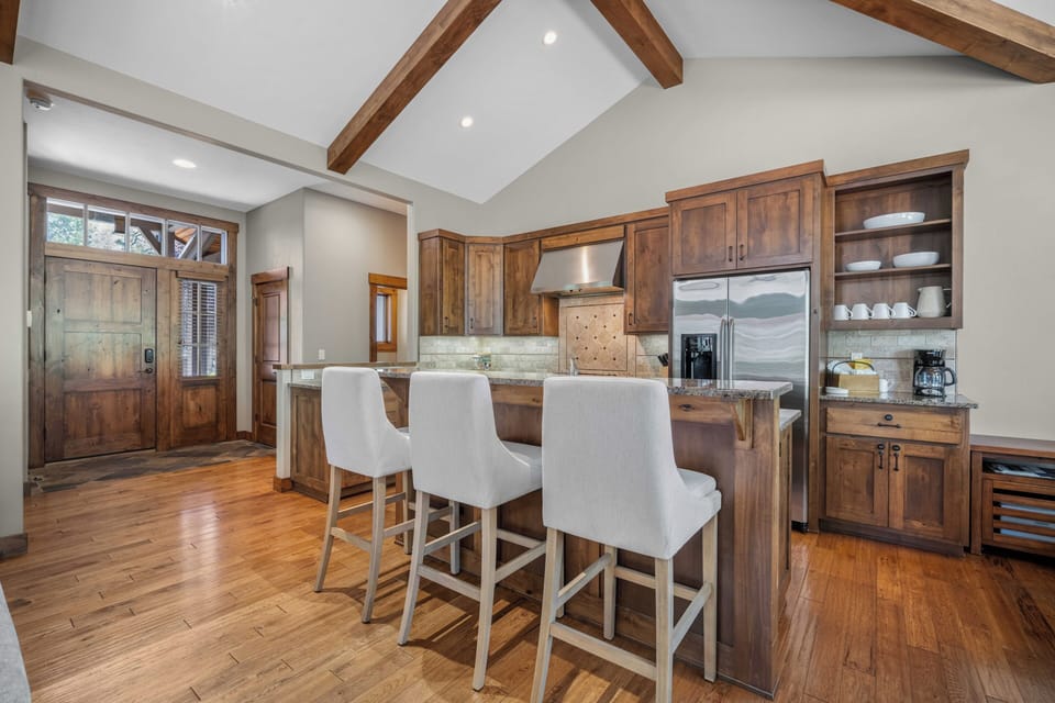 Gather around the spacious kitchen island with stunning wood cabinetry and vaulted ceilings accented by exposed beams. Modern stainless appliances, granite countertops, and warm hardwood floors create your ideal space for cooking and conversation.