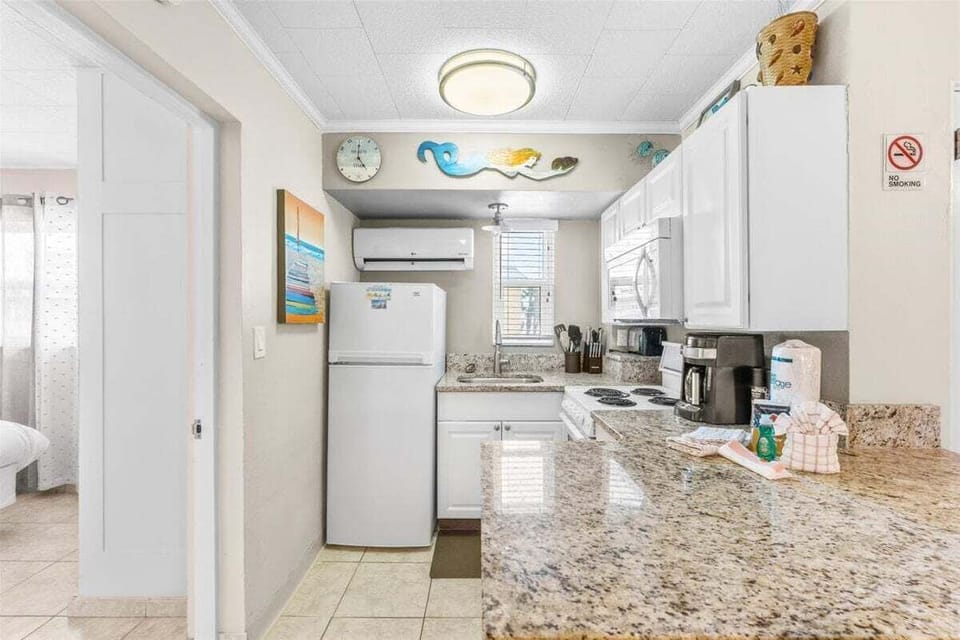 Fully equipped kitchen with white cabinets, granite counters, stove, microwave, fridge, and coffee maker — everything you need for a home-cooked beach meal.